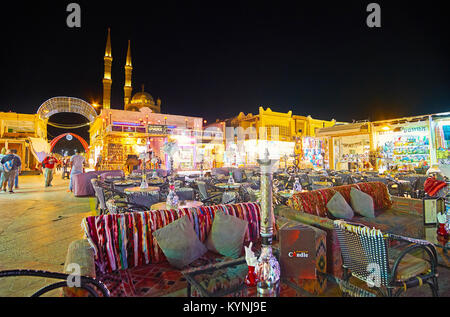 SHARM EL SHEIKH, EGYPT- DECEMBER 15, 2017: The tables of restaurant in Old Souk with shishas, numerous souvenir stalls and minarets of Shaba Mosque ar Stock Photo