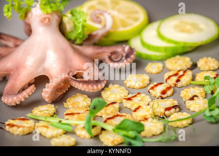 close up of octopus served with lime, corn, cucumber and sprig of pea leaves on plate Stock Photo