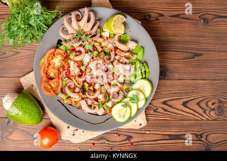 top view of salad with tentacles of octopus, lime, avocado and lettuce, decorated lime, cucumber, tomato, sprigs of pea leaves and dry peppers, natura Stock Photo