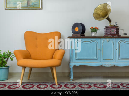 Vintage interior of retro orange armchair, vintage wooden light blue sideboard, old phonograph (gramophone), vinyl records on background of beige wall Stock Photo