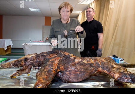 Trinwillershagen, Germany. 12th Jan, 2018. German Chancellor Angela Merkel (CDU) stands next to butcher Andre Teuerung and waits for the first piece of roast wild boar during the New Year's Reception of the state counsil of the district Vorpommern-Ruegen in Trinwillershagen, Germany, 12 January 2018. Merkel has been representing the electoral district Stralsund-Greifswald-Ruegen-Vorpommern since 1990 in the German Bundestag with a direct mandate. Credit: Stefan Sauer/dpa/Alamy Live News Stock Photo