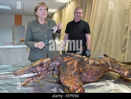 Trinwillershagen, Germany. 12th Jan, 2018. German Chancellor Angela Merkel (CDU) stands next to butcher Andre Teuerung and waits for the first piece of roast wild boar during the New Year's Reception of the state counsil of the district Vorpommern-Ruegen in Trinwillershagen, Germany, 12 January 2018. Merkel has been representing the electoral district Stralsund-Greifswald-Ruegen-Vorpommern since 1990 in the German Bundestag with a direct mandate. Credit: Stefan Sauer/dpa/Alamy Live News Stock Photo