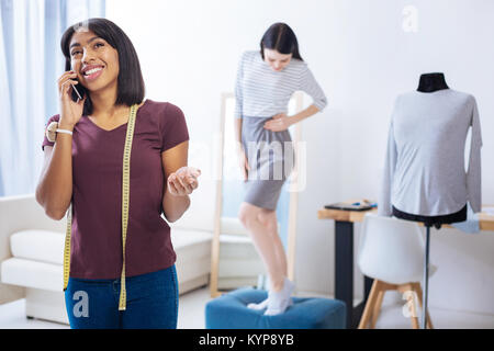 Emotional tailor talking on the phone with the client behind her back Stock Photo