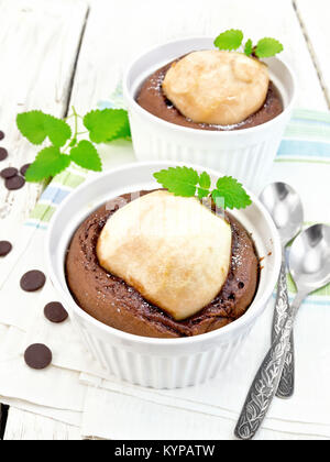 Two white dessert bowl with chocolate and pear, spoon, mint on a napkin on a wooden board Stock Photo