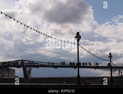 Pedestrians crossing over the Millennium foot bridge over the River Thames, London with classical London street lamps and rows of street bulbs Stock Photo