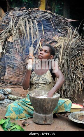 Africa. Jungle of the Central-African Republic. Baka woman cooks food, crushing a flour in a mortar Stock Photo