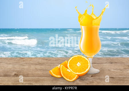 orange juice in glass and fresh orange fruit on the beach table. Orange juice splash. Blurred ocean or sea background. Healthy drink, summer holiday v Stock Photo