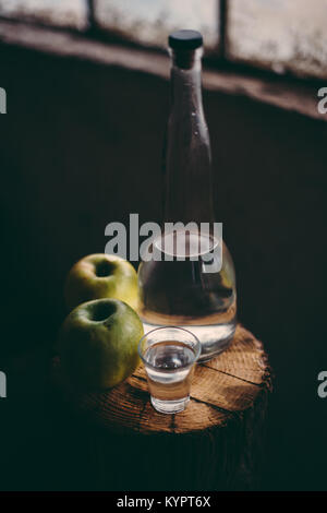 Apple brandy, rustic retro atmosphere. Bottle and single shot glass with alcohol drink and two green apple fruit. Stock Photo
