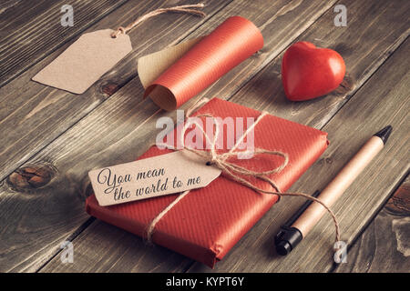 Packed present, wrapping  paper, paper, cardboard tags and and stone heart on rustic wooden table. Valentine's day concept. Text on the tag: 'You mean Stock Photo