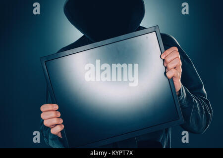 Cybersecurity, hacker holding blank computer monitor screen with hoodie and obscured face Stock Photo