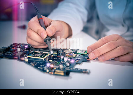 Tech fixes motherboard in service center. Shallow DOF, focus on hands, image is toned with extra light effects Stock Photo