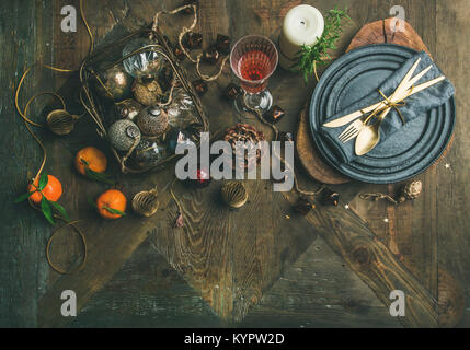 Christmas or New Year’s eve holiday table setting. Flat-lay of plates, silverware, shampaigne in glass, candle and toy festive decorations over vintah Stock Photo