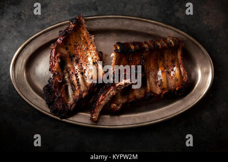 Grilled pork spare ribs cooked with balsamic vinegar and honey sauce on vintage metallic tray. Dark rustic background. Stock Photo
