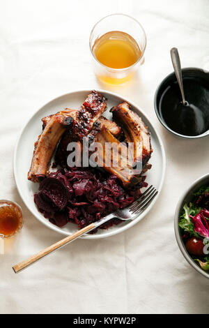 Grilled pork ribs cooked with balsamic vinegar and honey sauce, garnished with red wine braised red cabbage with beets on white plate. White linen bac Stock Photo