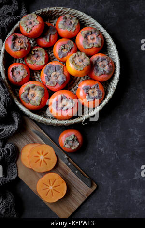 Fresh Persimmons in a bowl, and on a chopping board Stock Photo