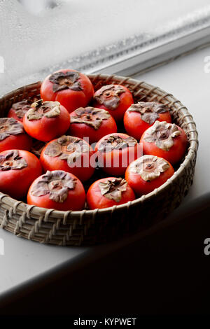 Persimmons in a basket on a window ledge Stock Photo