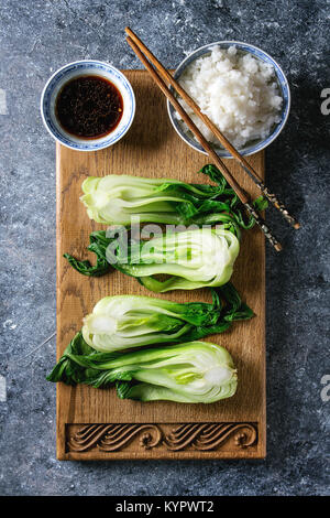 Stir fried bok choy or chinese cabbage with soy sauce and bowl of rice served on decorative wooden cutting board with chopsticks over dark texture bac Stock Photo