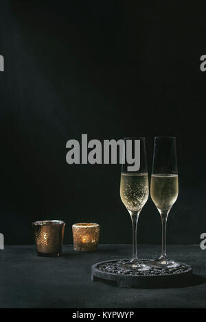 Two glasses of white champagne served on black wooden decorative board with candles over dark texture background. Copy space Stock Photo
