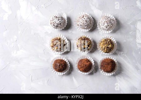 Variety of homemade dark chocolate truffles with cocoa powder, coconut, walnuts in row over gray texture background. Top view, copy space. Stock Photo