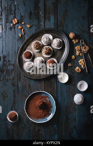 Variety of homemade dark chocolate truffles with cocoa powder, coconut, walnuts on vintage tray over old dark blue wooden background. Top view, space. Stock Photo