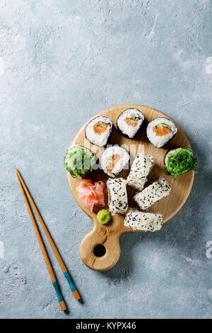 Homemade sushi rolls set with salmon, sesame seeds serving on wood serving board with pink pickled ginger, soy sauce, wasabi, seaweed salad, chopstick Stock Photo