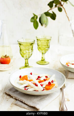 Jicama Persimmon Pomegranate Salad with Guava Chevre Vinaigrette served with white wine. Photographed on a rustic white background. Stock Photo