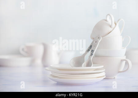 Stack of teatime tableware. Porcelain cups and saucers on a white wooden background. High key food photography. Stock Photo