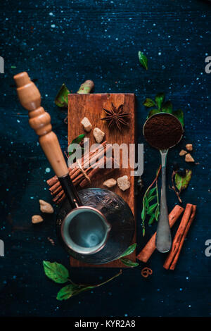 Steaming cezve with hot coffee on dark background with beans and cinnamon. Top view of coffee preparation process. Stock Photo