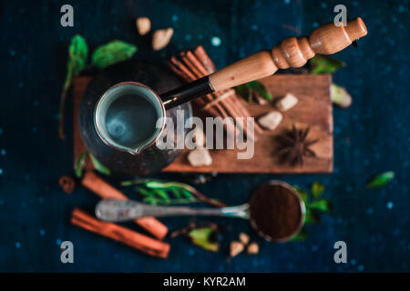 Steaming cezve with hot coffee on dark background with beans and cinnamon. Top view of coffee preparation process. Stock Photo