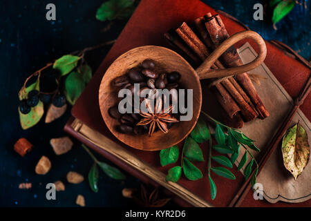 Wooden bowl with coffee beans on a dark background with anise stars, cinnamon, brown sugar and leaves. Vintage still life with barista utensils. Brewi Stock Photo