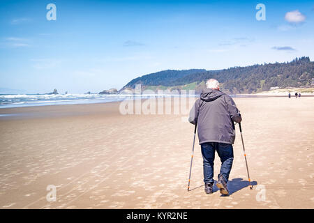 Old man getting exercise walking with trekking poles on the beach. Copy space. Stock Photo