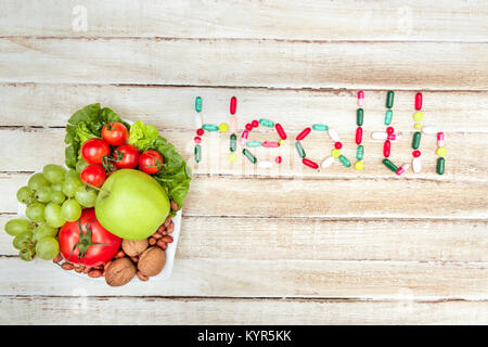 top view of fresh organic vegetables and fruits on plate with health word made of pills on wooden surface Stock Photo
