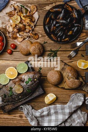 Top view of assorted seafood and baked fish with bread and tomatoes on wooden table Stock Photo