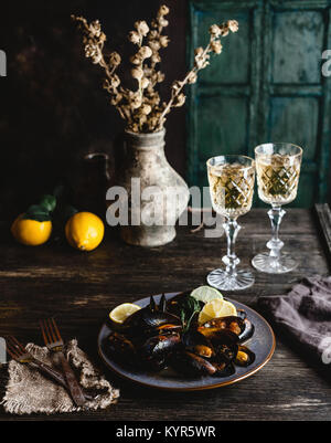 Cooked mussels with shells served on plate with two glasses of white wine on wooden table Stock Photo
