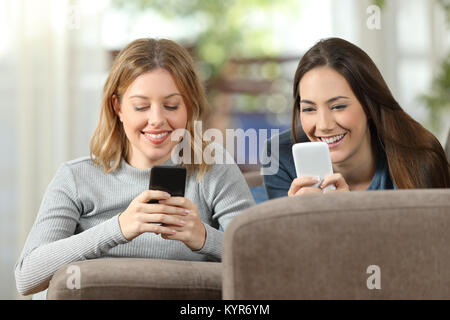 Front view of two happy roommates using two smart phones lying on a couch in the living room at home Stock Photo