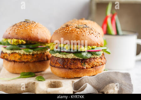 Healthy baked sweet potato burger with whole grain bun, guacamole, vegan mayonnaise and vegetables on a board. Vegetarian food concept, light backgrou Stock Photo