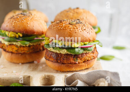 Healthy baked sweet potato burger with whole grain bun, guacamole, vegan mayonnaise and vegetables on a board. Vegetarian food concept, light backgrou Stock Photo