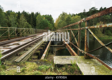 Old abandoned railroad bridge above river in Poland; vintage motorbike in background. Vintage industrial landscape Stock Photo