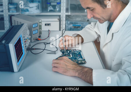 Senior male tech works in hardware repair facility fixing faulty motherboard, Shallow DOF, focus on the hand with the tool. This image is toned. Stock Photo