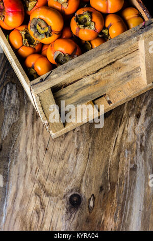 Box of fresh fruits persimmon kaki on old wooden background. Copy space Stock Photo