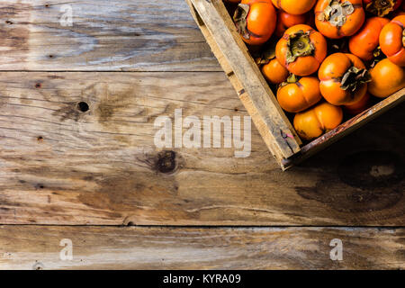 Box of fresh fruits persimmon kaki on old wooden background. Copy space Stock Photo