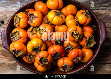 Pot of fresh fruits persimmon kaki on old wooden background. Copy space Stock Photo