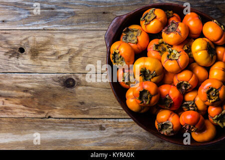 Pot of fresh fruits persimmon kaki on old wooden background. Copy space Stock Photo