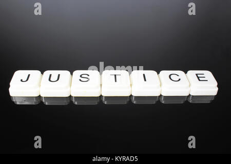 Justice text word title caption label cover backdrop background. Alphabet letter toy blocks on black reflective background. White alphabetical letters. White educational toy block with words on mirror table. Stock Photo