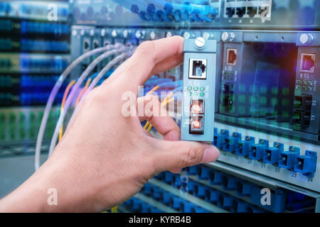 man working in network server room with Fiber Optic cables connected to optic ports Stock Photo