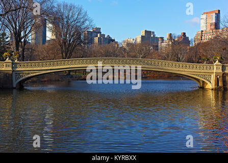 Bow Bridge at sunny morning in Central Park, New York City. Landscape of the park with lake and urban Manhattan skyscrapers on horizon in winter. Stock Photo