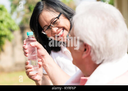 Careful senior woman giving a bottle of water to her partner out Stock Photo