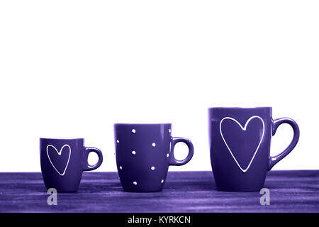 Three red coffee cups, with hearts and polka dots, standing on black wooden surface with place for text. Coffee for St. Valentine's Day. White backgro Stock Photo