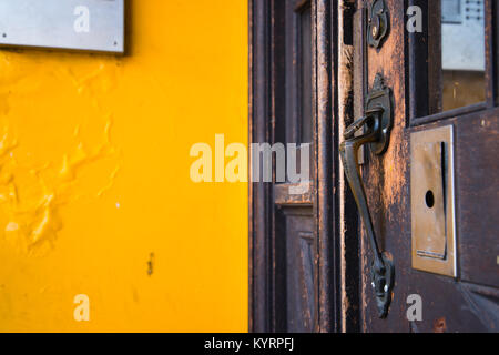 An old bronze carved door handle on the same old wooden door, covered with dark stain, in a building with yellow walls and obsolete electronics Stock Photo