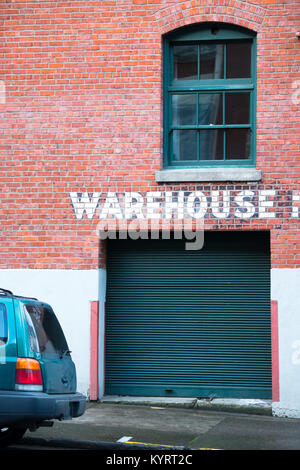 Corrugated gate in a brick building several floors with an old window and an inscription warehouse on the surface of a brick wall Stock Photo